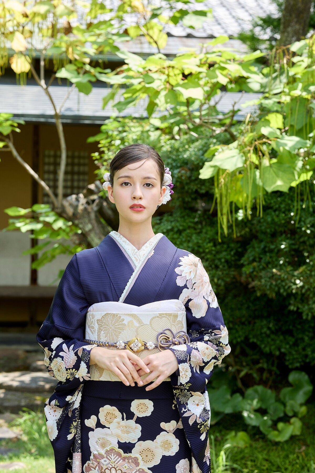 深いネイビーに白い花柄をあしらった振袖で庭園に立つ女性