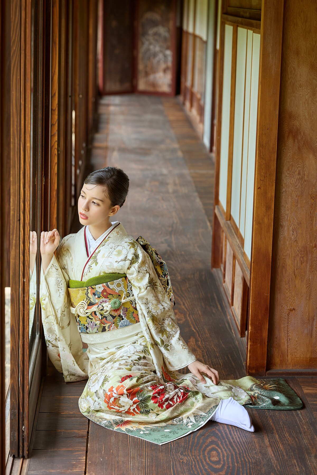 淡い色の振袖で伝統的な廊下に座る女性